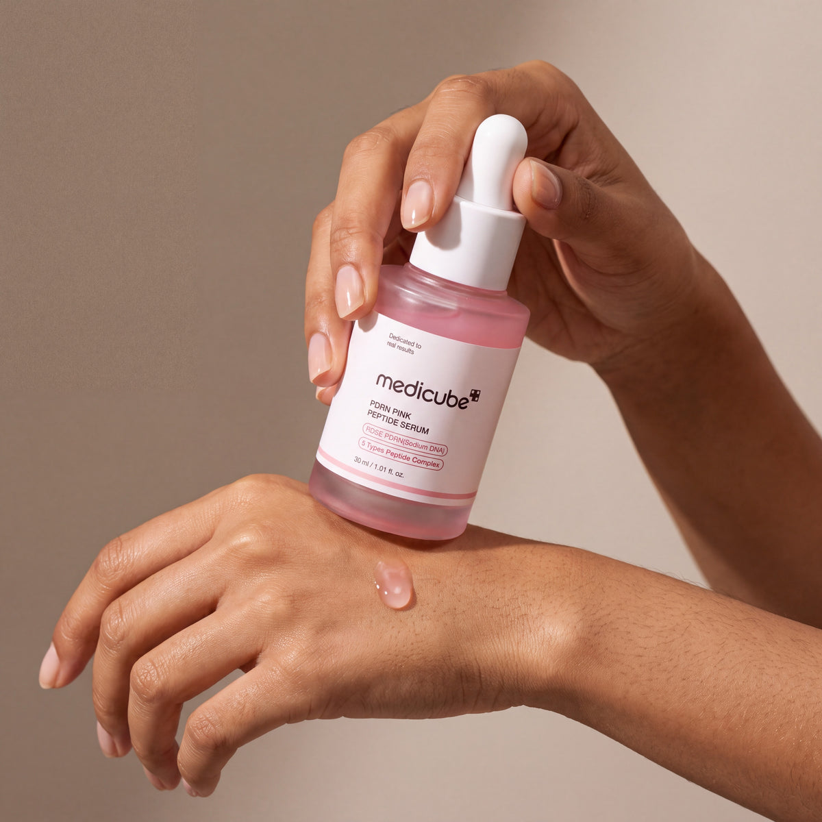 Medicube PDRN Pink Peptide Serum held in hands, editorial studio shot