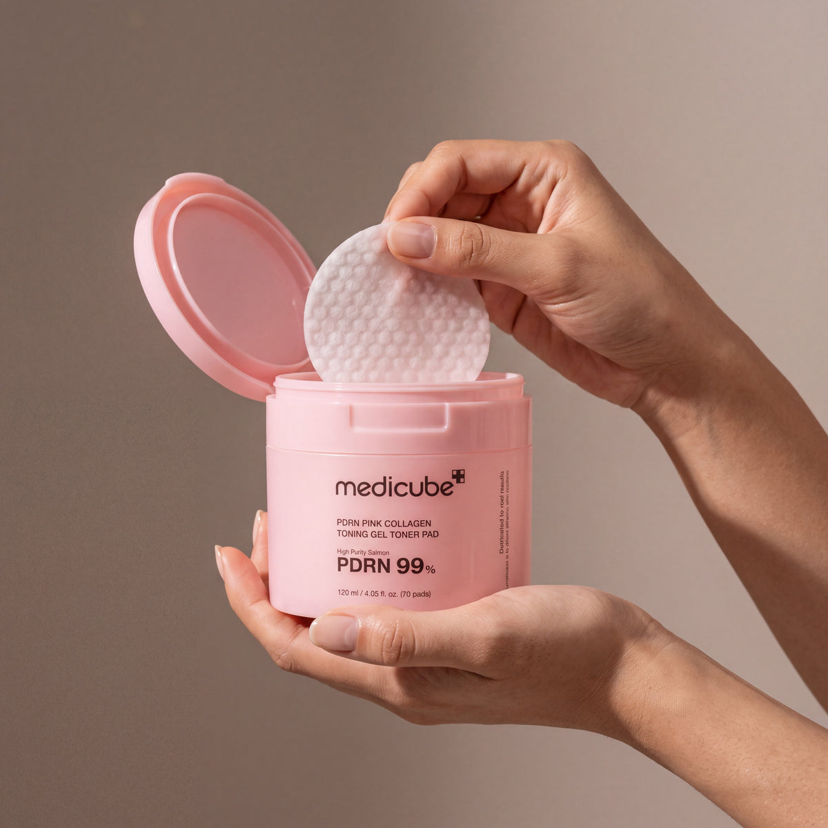 Medicube PDRN Pink Collagen Toning Gel Toner Pad held in hands, editorial studio shot
